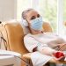 Portrait of young woman in protective mask looking at camera while lying on the couch and receiving a blood transfusion at hospital