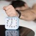 Annoyed sleepy man turning off alarm, hitting button on the clock by his fist after sleepless night, angry and frustrate sleeper feeling not rested and tired, lying in bed and wanting to sleep more