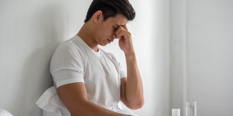 A man with migraines holds her hand by his nose in the bed.