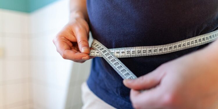 man measures her abdomen with a measuring tape