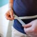 man measures her abdomen with a measuring tape