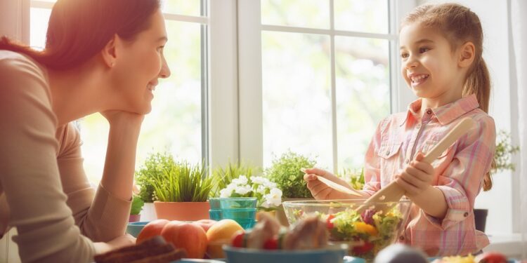 Happy family having dinner together sitting at the rustic wooden table. Mother and her daughter enjoying family dinner together.