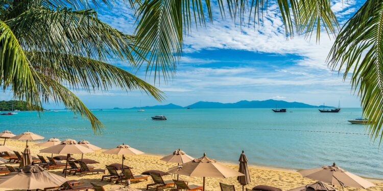 Beautiful tropical beach sea and ocean with coconut palm tree  and umbrella and chair on blue sky and white cloud for holiday vacation travel