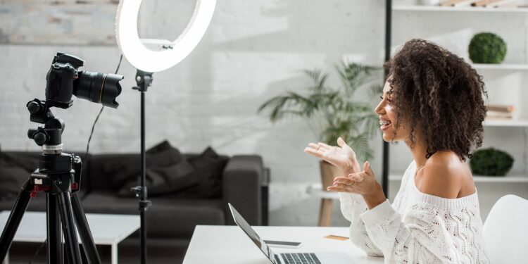 side view of happy african american influencer in braces gesturing near digital camera