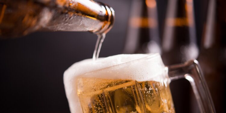 Glass bottles of beer with glass and ice on dark background