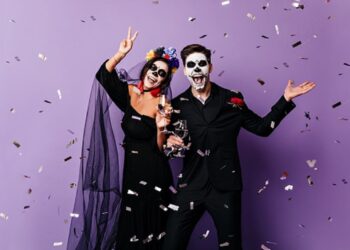 Active man and woman in costumes for Halloween dance on purple background among confetti