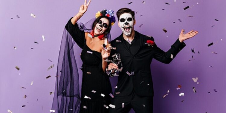 Active man and woman in costumes for Halloween dance on purple background among confetti