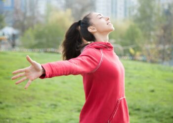 Profile portrait of happy sporty woman relaxing in park. Joyful female model relaxing, breathing fresh air outdoors with opened arms. Healthy active lifestyle concept