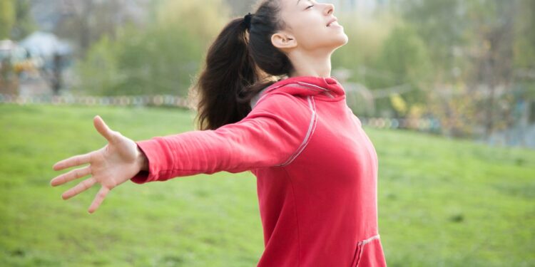 Profile portrait of happy sporty woman relaxing in park. Joyful female model relaxing, breathing fresh air outdoors with opened arms. Healthy active lifestyle concept
