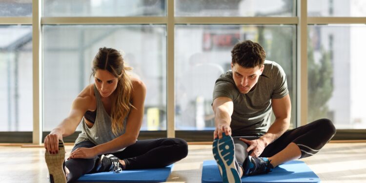 Young woman and man working out indoors. Two people streching their legs on the floor of a gym.