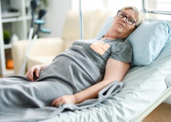Elderly age woman laying on a bed in a nursing home covered with a blanket.