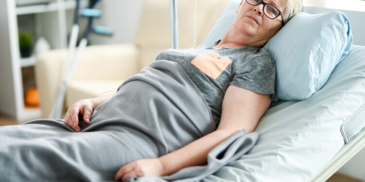 Elderly age woman laying on a bed in a nursing home covered with a blanket.