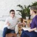 Picture of frustrated young Caucasian man wearing sweater and eyeglasses sitting on comfortable couch, sharing his personal problems with middle aged female counselor during therapy session