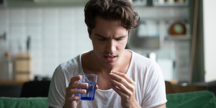 Millennial man taking antibiotic antidepressant painkiller pill medication to relieve pain at home, young guy feeling sick ill suffering from headache, stress or flu, emergency treatment concept
