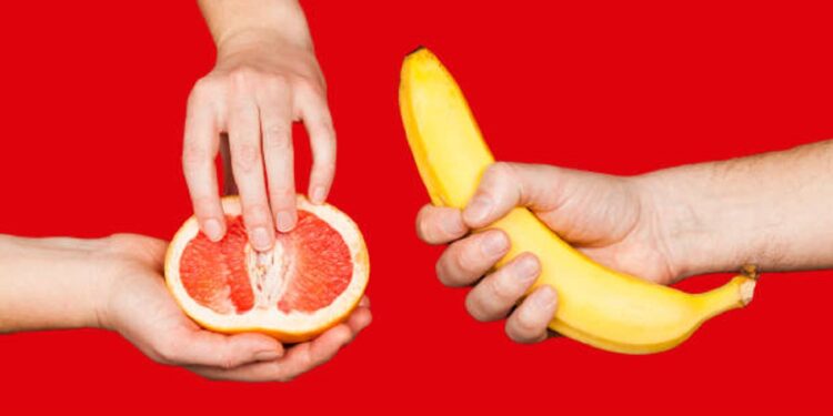 Banana and grapefruit in hands isolated on a red background as a symbol of male and female masturbation. Games with the clitoris and touching the penis. Stimulation and orgasm.