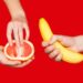 Banana and grapefruit in hands isolated on a red background as a symbol of male and female masturbation. Games with the clitoris and touching the penis. Stimulation and orgasm.