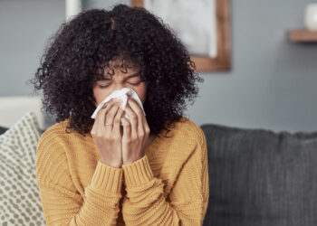 Shot of a young woman blowing her nose with a tissue at home