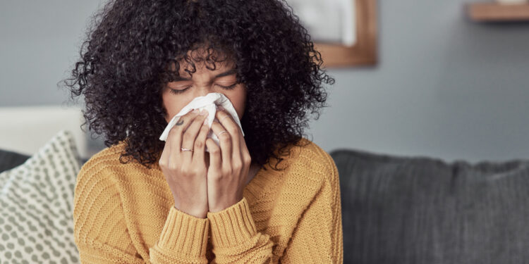 Shot of a young woman blowing her nose with a tissue at home