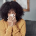 Shot of a young woman blowing her nose with a tissue at home