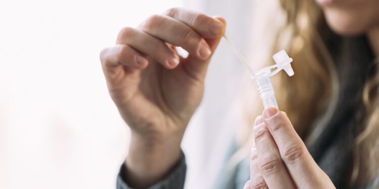 Side view of woman placing swab into the antigen test extraction tube