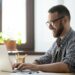 Happy male office worker smiling typing message at laptop, chatting with friends, writing positive email or consulting client online. Concept of laugher, positive work atmosphere, help and assistance