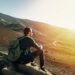 Man with rucksack sitting on rock at sunset on background of volcano Etna mountain in Sicily