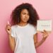 Displeased stressful dark skinned woman looks at periods calendar with marked red crosses, has painful menstruation, holds tampon for good protection. People, women health and hygiene concept