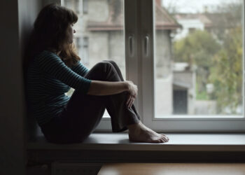 Sad young woman sitting on the window