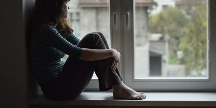 Sad young woman sitting on the window