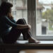 Sad young woman sitting on the window