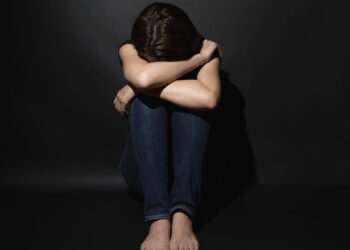 Depressed young woman with head in hands sitting lonely.