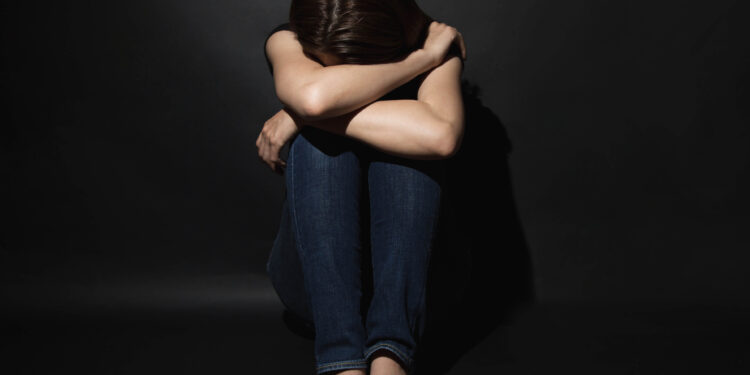 Depressed young woman with head in hands sitting lonely.
