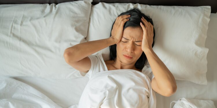 Unhappy exhausted mature woman with closed eyes lying in bed, touching temples close up, tired female suffering from headache or migraine, feeling unwell, suffering from insomnia, lack of sleep