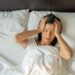 Unhappy exhausted mature woman with closed eyes lying in bed, touching temples close up, tired female suffering from headache or migraine, feeling unwell, suffering from insomnia, lack of sleep