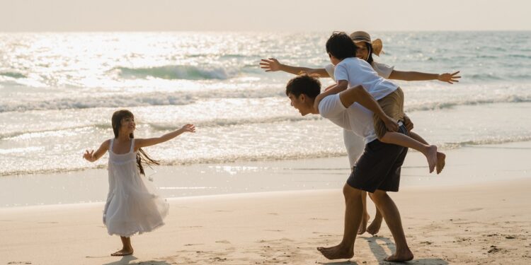 Asian young happy family enjoy vacation on beach in the evening. Dad, mom and kid relax playing together near sea when sunset while travel holiday. Lifestyle travel holiday vacation summer concept.