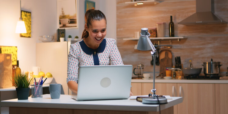 Excited woman feel ecstatic reading great online news on laptop working from home kitchen. Happy employee using modern technology network wireless doing overtime studying writing, searching