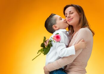 Young kid giving red rose to his mom on orange background