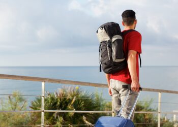 Rear view of man traveling with backpack and suitcase