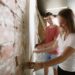 Young couple doing apartment repair together themselves. Married man and woman doing home makeover or renovation. Concept of relations, family, love. Measuring the wall, preparing for design.