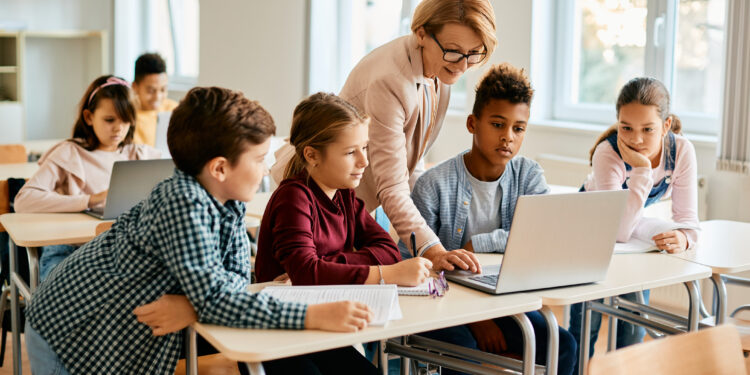 Elementary teacher and her students using laptop during computer class at school.