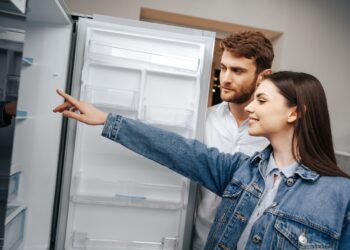 Young couple selecting new refrigerator in household appliance store, close up