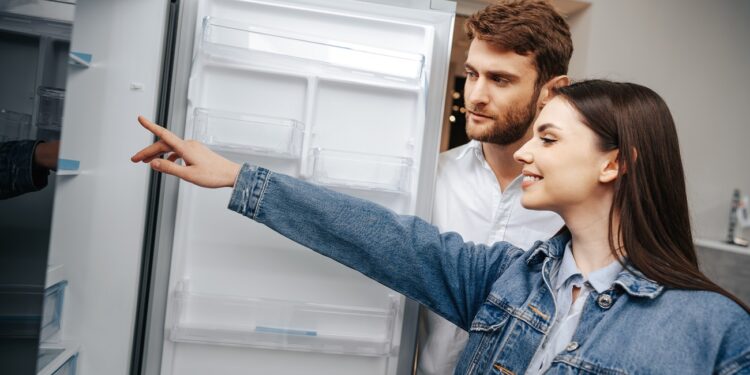 Young couple selecting new refrigerator in household appliance store, close up