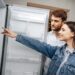 Young couple selecting new refrigerator in household appliance store, close up