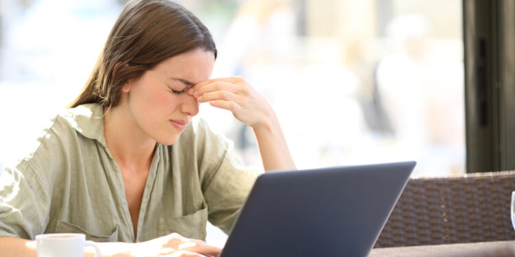 Fatigued woman suffering eyestrain working with a laprop sitting in a coffee shop