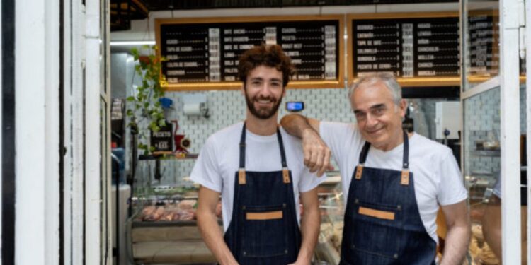 Father and so owners of a butcher shop standing at the entrance smiling at camera very happy