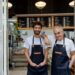 Father and so owners of a butcher shop standing at the entrance smiling at camera very happy