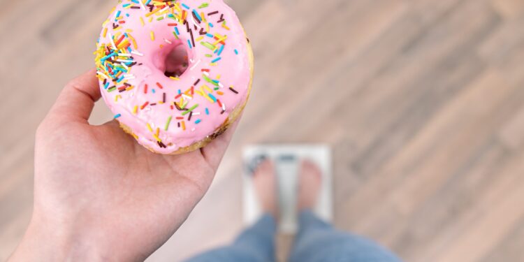 A woman stands on the scales, holds a donut in her hands, the concept of diet, weight gain, weight loss, proper nutrition, sweet.