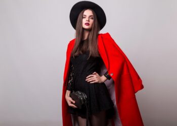 Fashionable woman in  red coat and black hat posing in studio, looking at camera. cold season. Autumn or winter look.