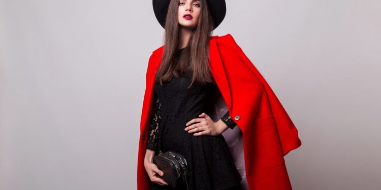 Fashionable woman in  red coat and black hat posing in studio, looking at camera. cold season. Autumn or winter look.
