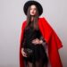 Fashionable woman in  red coat and black hat posing in studio, looking at camera. cold season. Autumn or winter look.
